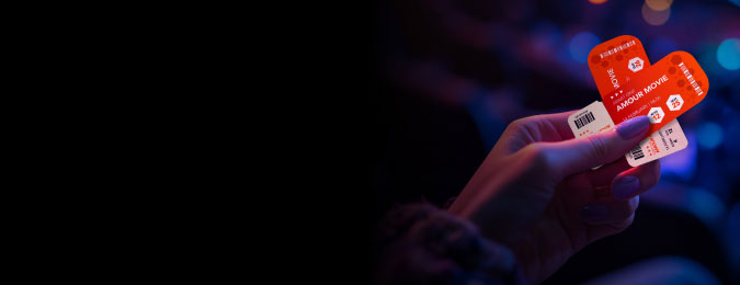 A hand holding two red tickets in the shape of a heart